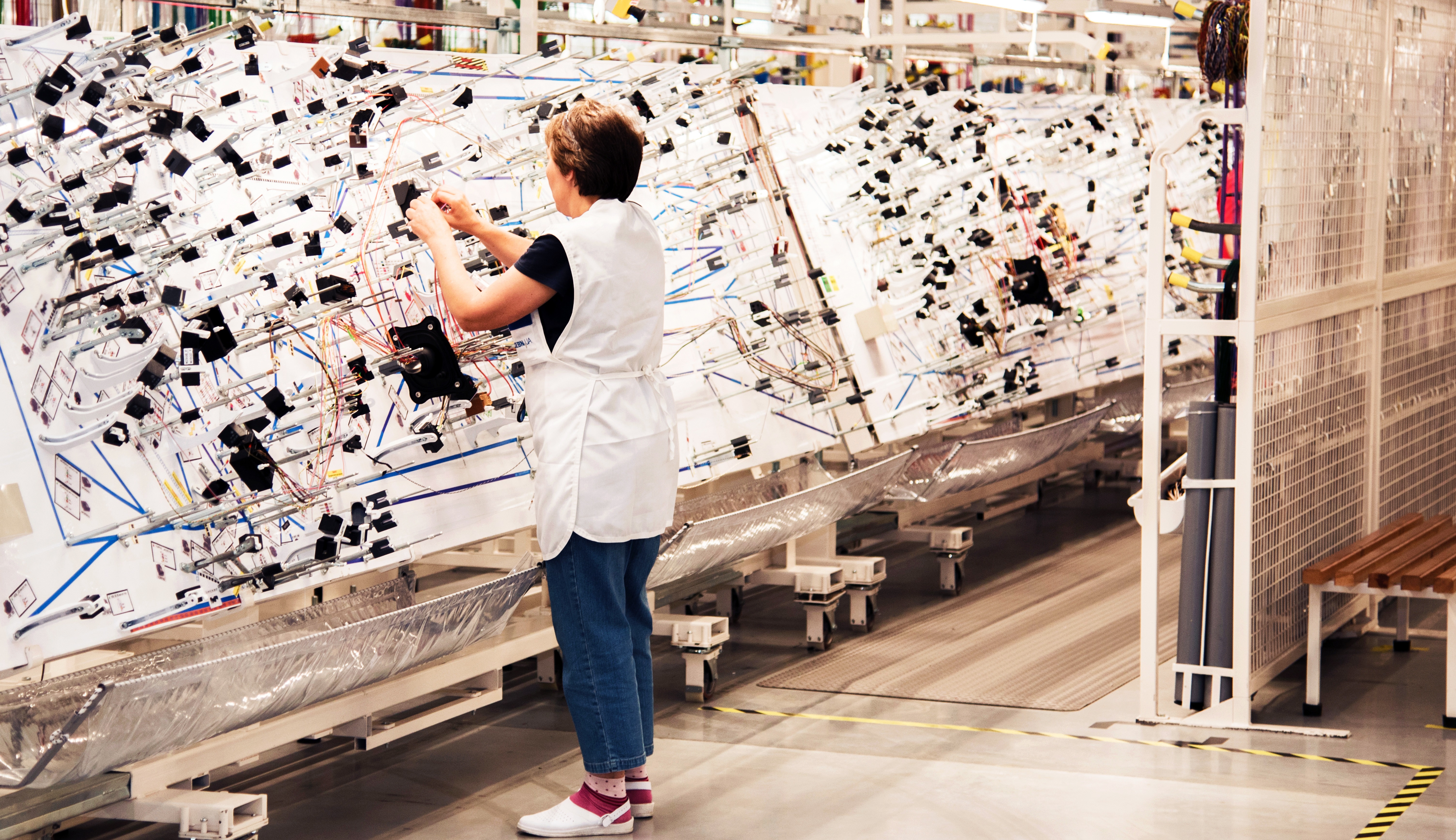 A worker in a production room with stands for manufacturing electric wiring for cars at a modern plant